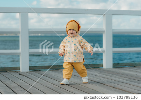 A toddler in a yellow jacket and pants walks on the pier 102799136