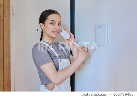 Teenage girl holding intercom handset while talking to guest Teenage girl holding intercom handset while talking to guest 102799492