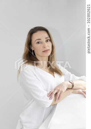 Portrait of Charming Beautician in White Lab Coat Looking at Camera With Smile, Near Couch, Looking at Camera in Spa Salon. Vertical Plane 102802621