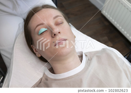 Topview Eyelash Care Treatment Procedures: Laminating, Curling, Staining, Extension For Lashes. Young Woman Lying On Couch Under Process Of Lash Lift, Nourishing Treatment With Keratin. Horizontal Topview Eyelash Care Treatment Procedures: Laminating, Curling, Staining, Extension For Lashes. Young Woman Lying On Couch Under Process Of Lash Lift, Nourishing Treatment With Keratin. Horizontal 102802623