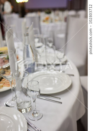 Classy table with a bouquet. Luxury dining set with cutlery, serviette, crockery and covered with a tablecloth in restaurant. Classy table with a bouquet. Luxury dining set with cutlery, serviette, crockery and covered with a tablecloth in restaurant. 102803712