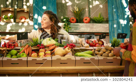 People enjoying shopping at local farmers market, checking fresh farm produce. Young diverse couple standing at farming stand with various homegrown organic fruits and vegetables. 102804241
