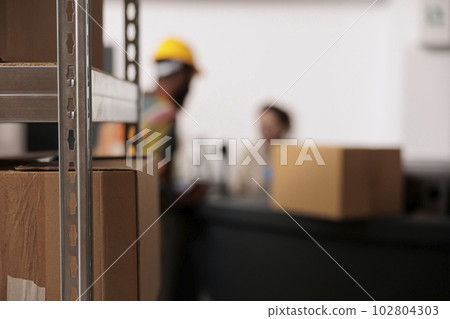 Selective focus of employees looking at cardboard box during inventory, preparing packages for clients orders. Small business diverse team working at delivery process analyzing checklist in warehouse Selective focus of employees looking at cardboard box during inventory, preparing packages for clients orders. Small business diverse team working at delivery process analyzing checklist in warehouse 102804303