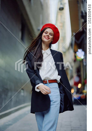 Fashion woman smile with teeth portrait walking tourist in stylish clothes in jacket with red lips walking down narrow city street flying hair, travel, cinematic color, retro vintage style. 102808438