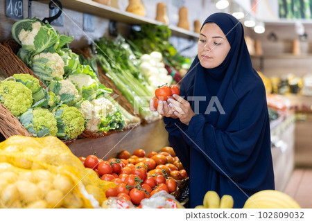 Young female shopper in muslim dress choosing tomatoes in supermarket Young female shopper in muslim dress choosing tomatoes in supermarket 102809032