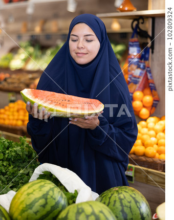 Girl in veil carefully chooses fresh watermelon in supermarket 102809324