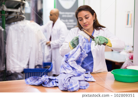 Focused woman drycleaner removing spots and stains Focused woman drycleaner removing spots and stains 102809351