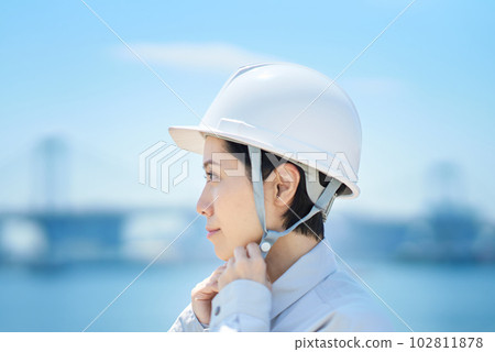 A woman wearing work clothes and checking a helmet 102811878