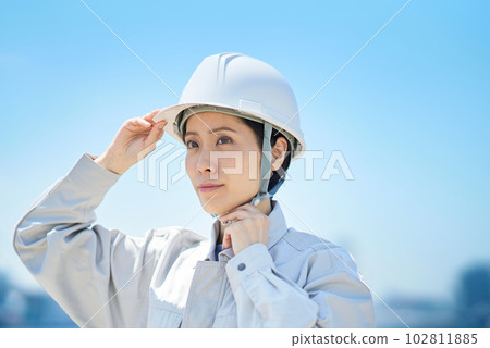 A woman wearing work clothes and checking a helmet A woman wearing work clothes and checking a helmet 102811885