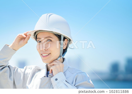 A woman wearing work clothes and checking a helmet A woman wearing work clothes and checking a helmet 102811886