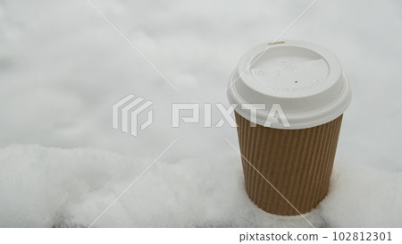 Hot warming drink in Eco paper cup. Mock up Cardboard coffee or tea Cup in the snow in winter day. Copy space zero waste recycle cup white snow-covered field 102812301