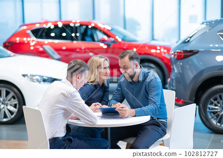 Happy caucasian couple signs a contract for the purchase of a car salon. Happy caucasian couple signs a contract for the purchase of a car salon. 102812727