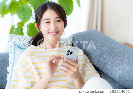 在房間裡操作智慧型手機的年輕女子 在房間裡操作智慧型手機的年輕女子 102814691