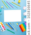 Top view arrangement album with white sheets and pens, pencils, paper clips and other office supplies on blue background 102816645