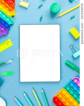 Top view arrangement album with white sheets and pens, pencils, paper clips and other office supplies on blue background 102816650