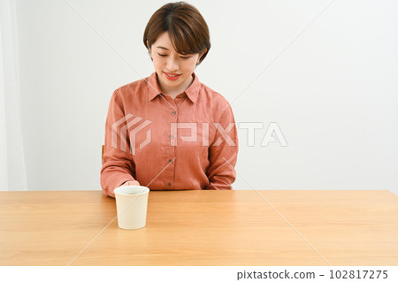 桌邊端著咖啡杯的年輕女子 桌邊端著咖啡杯的年輕女子 102817275