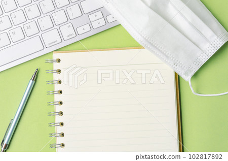 The Open blank diary and keyboard computer with disposable face mask on green background. 102817892
