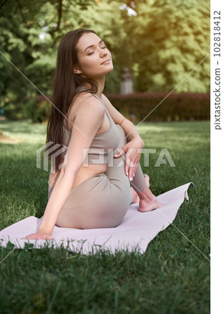 A young woman with a slim figure and long hair practices yoga in the park. Concept of a healthy lifestyle. A young woman with a slim figure and long hair practices yoga in the park. Concept of a healthy lifestyle. 102818412