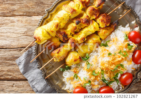 Grilled saffron chicken skewers with rice garnish close-up in a plate. horizontal top view 102821267