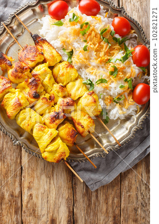 Joojeh Kabab or Jujeh chicken skewers with saffron served with Persian rice closeup on the plate on the table. Vertical top view Joojeh Kabab or Jujeh chicken skewers with saffron served with Persian rice closeup on the plate on the table. Vertical top view 102821271