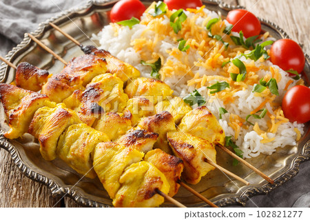 Grilled saffron chicken skewers with rice garnish close-up in a plate. horizontal Grilled saffron chicken skewers with rice garnish close-up in a plate. horizontal 102821277