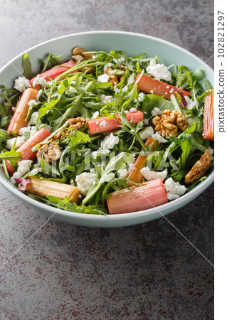 Fresh salad with rhubarb, arugula, goat cheese and walnuts close-up in a bowl. Vertical 102821297
