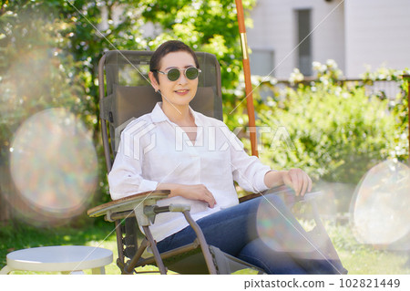 A middle-aged woman sitting on a chair in the garden and relaxing 102821449
