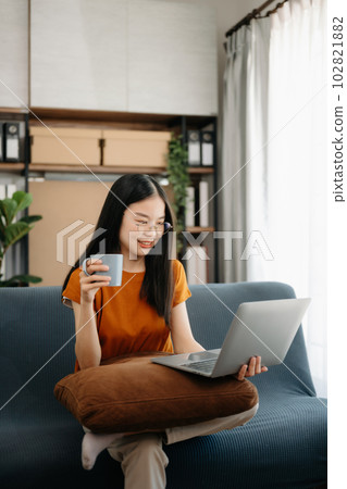 Female students note from the books at the Asian girl library sitting at the sofa using laptop computer and tablet to search an online informations. 102821882