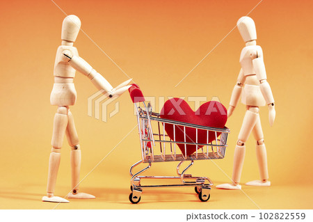 Dummy pushing a shopping cart with a red heart on orange background Dummy pushing a shopping cart with a red heart on orange background 102822559
