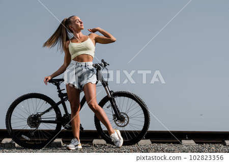Caucasian woman in denim shorts and top posing with a bike on a hot summer day. Caucasian woman in denim shorts and top posing with a bike on a hot summer day. 102823356