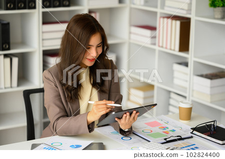 Beautiful female manager in stylish suit using digital tablet, searching online information at her workplace Beautiful female manager in stylish suit using digital tablet, searching online information at her workplace 102824400