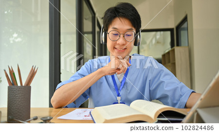 Asian male medical student in headphone reading books, preparing for university exams in library. Medical internship concept Asian male medical student in headphone reading books, preparing for university exams in library. Medical internship concept 102824486