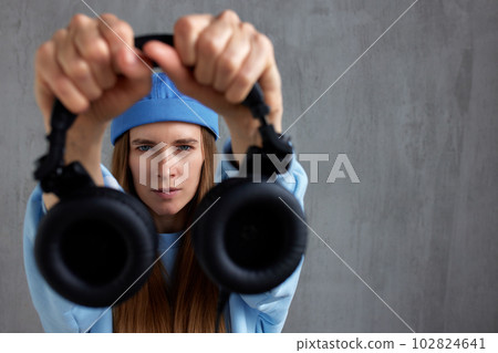 Young charming red-haired woman in a blue sweater and cap looks at the camera and holds DJ headphones in outstretched hands. Music and relaxation. Copy space. 102824641