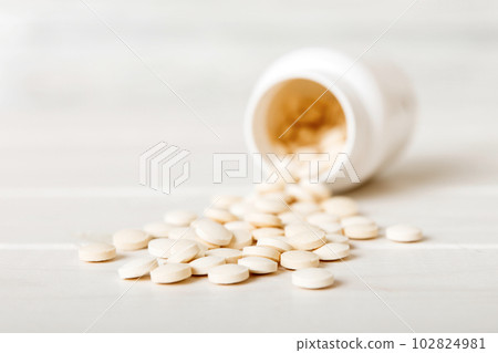 Medicine bottle and white pills spilled on a light background. Medicines and prescription pills flat lay background. White medical pills and tablets spilling out of a drug bottle 102824981