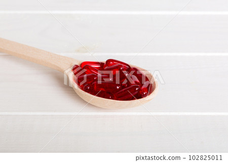 Vitamin capsules in a spoon on a colored background. Pills served as a healthy meal. Red soft gel vitamin supplement capsules on spoon Vitamin capsules in a spoon on a colored background. Pills served as a healthy meal. Red soft gel vitamin supplement capsules on spoon 102825011