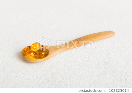 Vitamin omega capsules in a spoon on a colored background. Pills served as a healthy meal. Red soft gel vitamin supplement capsules on spoon 102825014