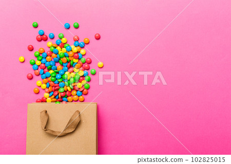 shopping paper gift bag in corner full of assorted traditional candies falling out on colored background with copy space. Happy Holidays sale concept 102825015