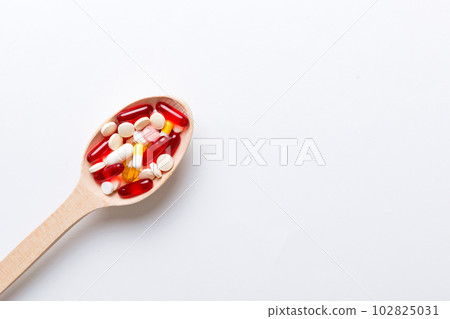 Vitamin capsules in a spoon on a colored background. Pills served as a healthy meal. Red soft gel vitamin supplement capsules on spoon Vitamin capsules in a spoon on a colored background. Pills served as a healthy meal. Red soft gel vitamin supplement capsules on spoon 102825031