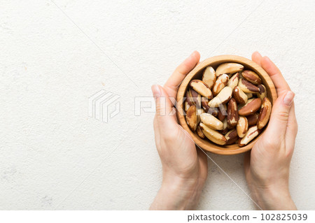 Woman hands holding a wooden bowl with brazil or bertholletia nuts. Healthy food and snack. Vegetarian snacks of different nuts 102825039