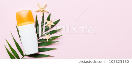 Sunscreen spray bottle. Bottle with sun protection cream and sea shells with tropical green leaf on color background, top view 102825180