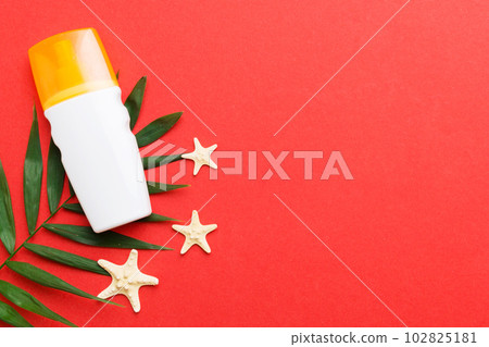 Sunscreen spray bottle. Bottle with sun protection cream and sea shells with tropical green leaf on color background, top view 102825181