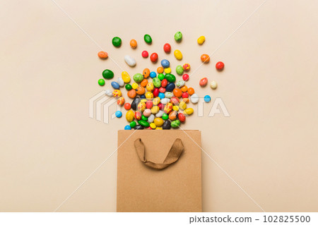 shopping paper gift bag in corner full of assorted traditional candies falling out on colored background with copy space. Happy Holidays sale concept shopping paper gift bag in corner full of assorted traditional candies falling out on colored background with copy space. Happy Holidays sale concept 102825500
