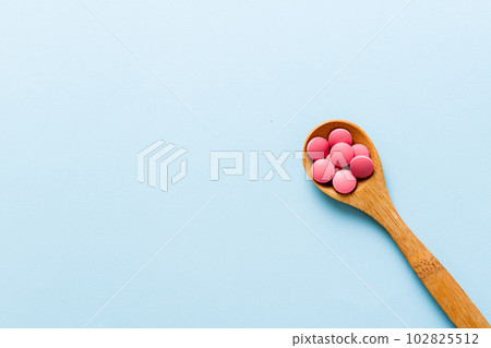 Vitamin capsules in a spoon on a colored background. Pills served as a healthy meal. Red soft gel vitamin supplement capsules on spoon 102825512