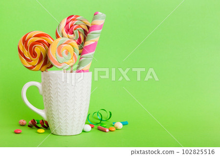 Colorful candies in cup on table on light background background. Large swirled lollipops. Creative concept of a jar full of delicious sweets from the candy store Colorful candies in cup on table on light background background. Large swirled lollipops. Creative concept of a jar full of delicious sweets from the candy store 102825516