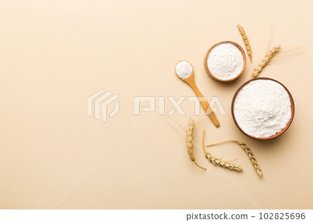 Flat lay of Wheat flour in wooden bowl with wheat spikelets on colored background. world wheat crisis Flat lay of Wheat flour in wooden bowl with wheat spikelets on colored background. world wheat crisis 102825696