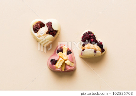 chocolate sweets in the form of a heart with fruits and nuts on a colored background. top view with space for text, holiday concept chocolate sweets in the form of a heart with fruits and nuts on a colored background. top view with space for text, holiday concept 102825708