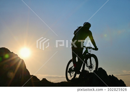 Silhouette Of A Cyclist Standing on Clif Against The Sun 102825926