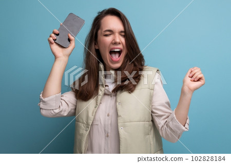 european young brunette woman in casual clothes holding her new smartphone in her hands 102828184