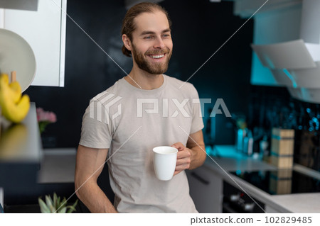 Man enjoying morning coffee in kitchen with modern interior, drinking fresh warm beverage at home. 102829485