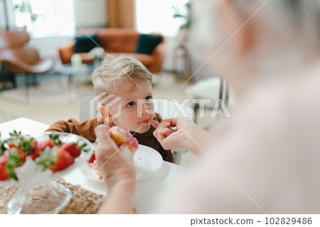 Little boy eating strawberry donut with his grandmother. Little boy eating strawberry donut with his grandmother. 102829486